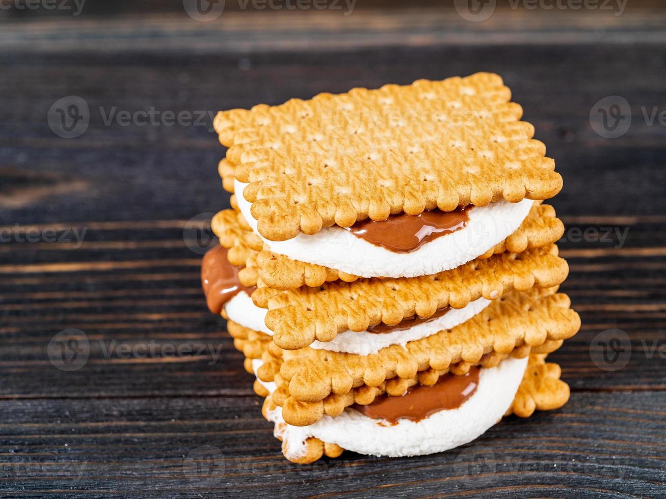 smores, sanduíches de marshmallow - biscoitos de chocolate doce americano tradicional na mesa de madeira escura, vista lateral foto