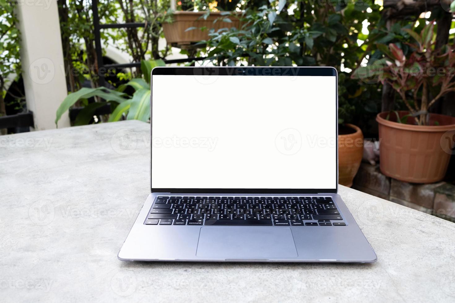 laptop com tela branca em branco na mesa branca. trabalho on-line em casa e trabalhar em qualquer lugar conceito. fundo de casa do jardim. foto