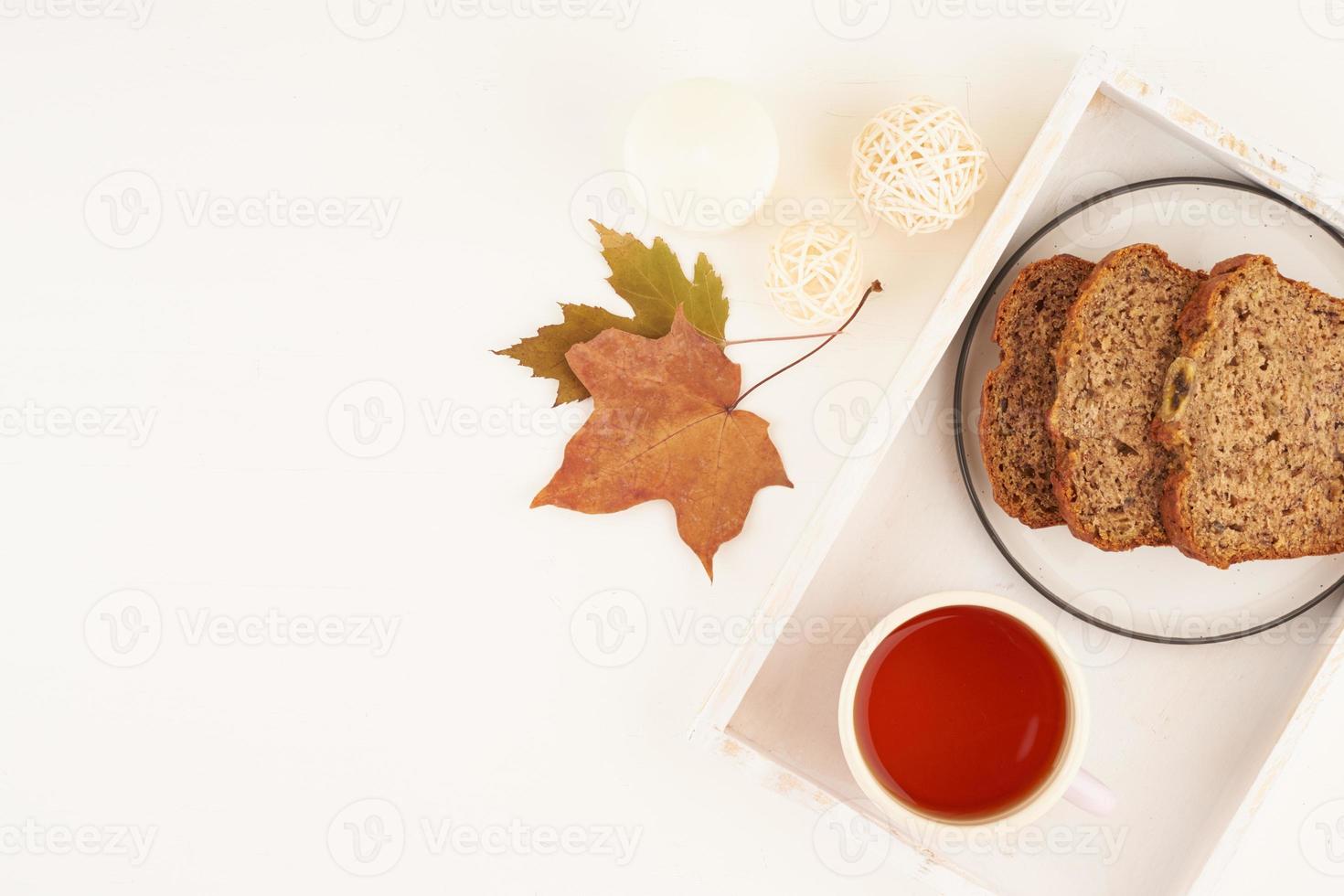 Outono alimentos-fatias de pão de banana, uma xícara de chá, folhas secas, mesa de madeira branca. inverno em casa aconchegante. vista lateral, copie o espaço foto