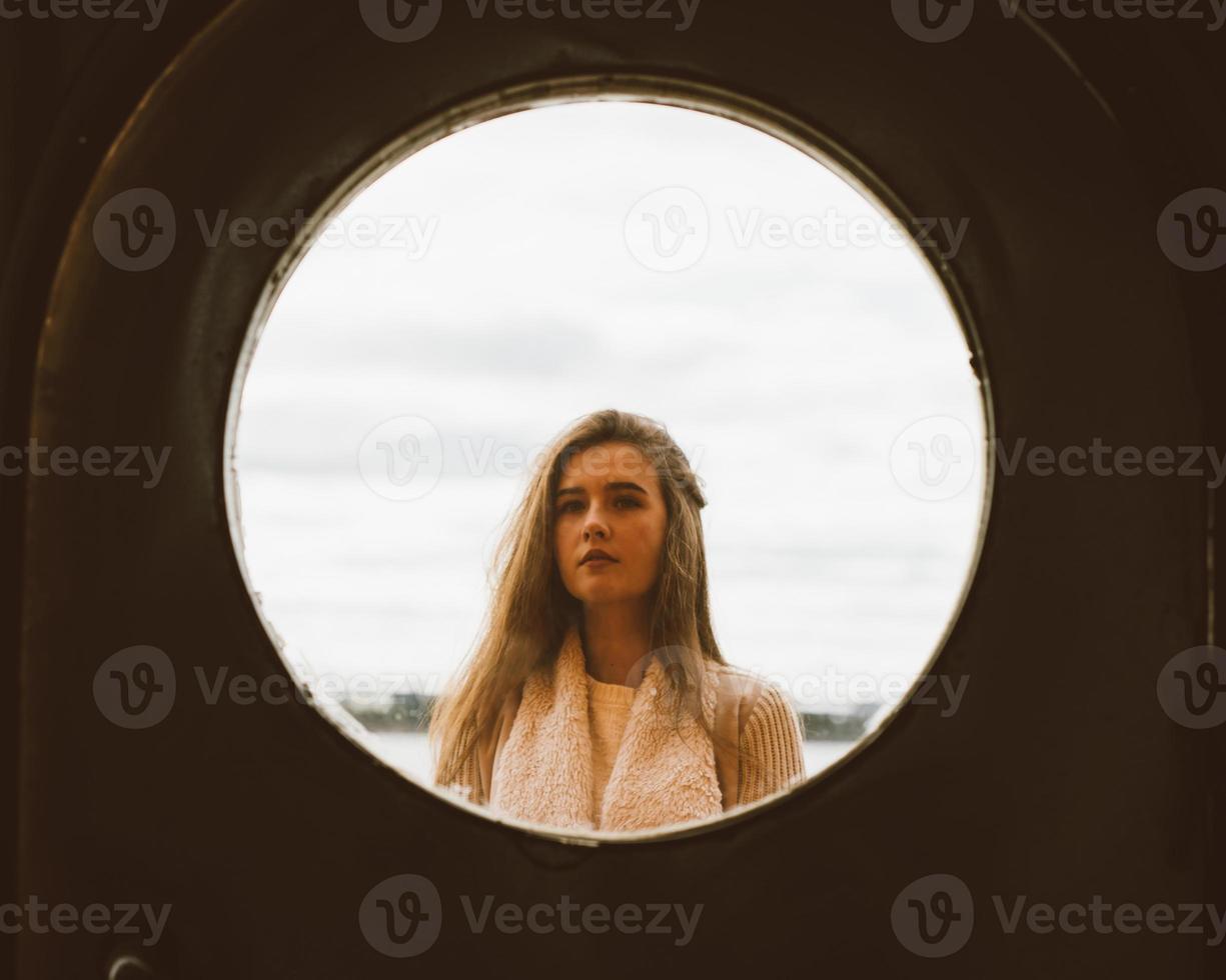 o rosto da jovem na janela de moldura redonda no fundo do mar, oceano, à beira-mar. retrato em círculo, retroiluminado foto