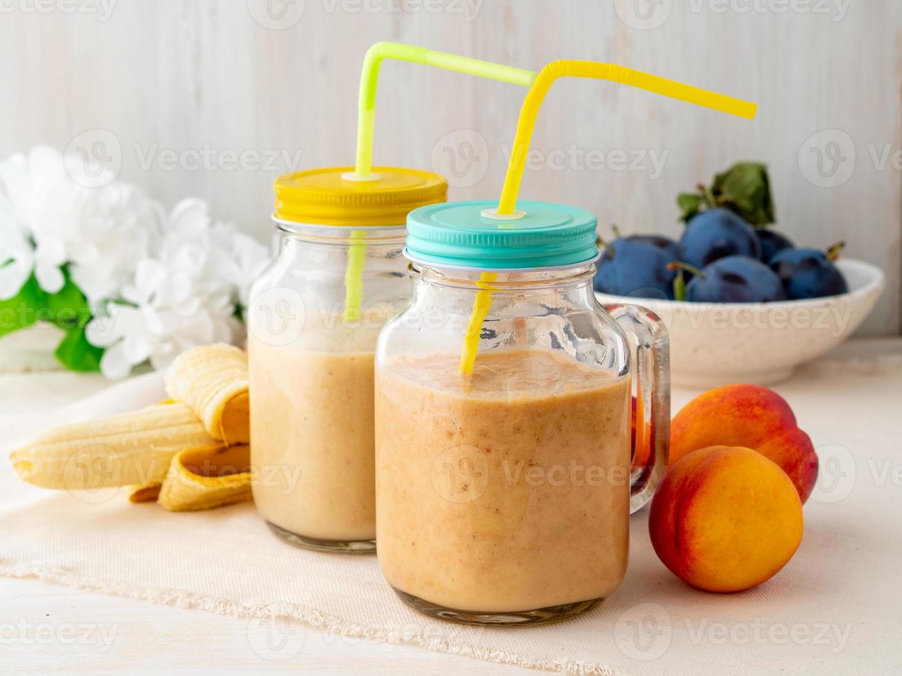 smoothie de nectarina de pêssego banana em dois potes, batidos de frutas frescas na mesa de madeira rústica branca, vista lateral foto