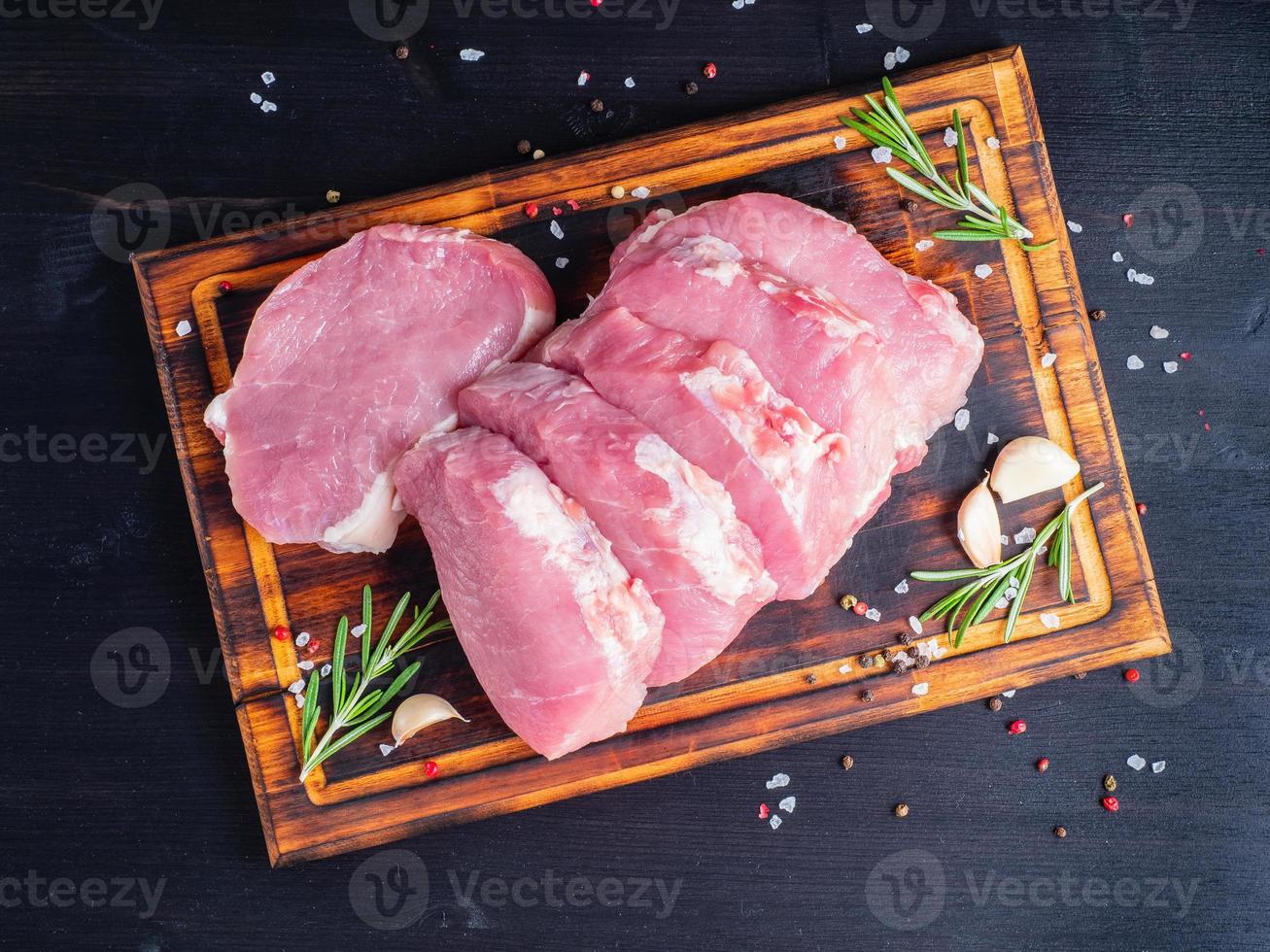 bife de porco, filé de carbonato cru em fundo escuro, carne com alecrim, temperos, vista superior foto