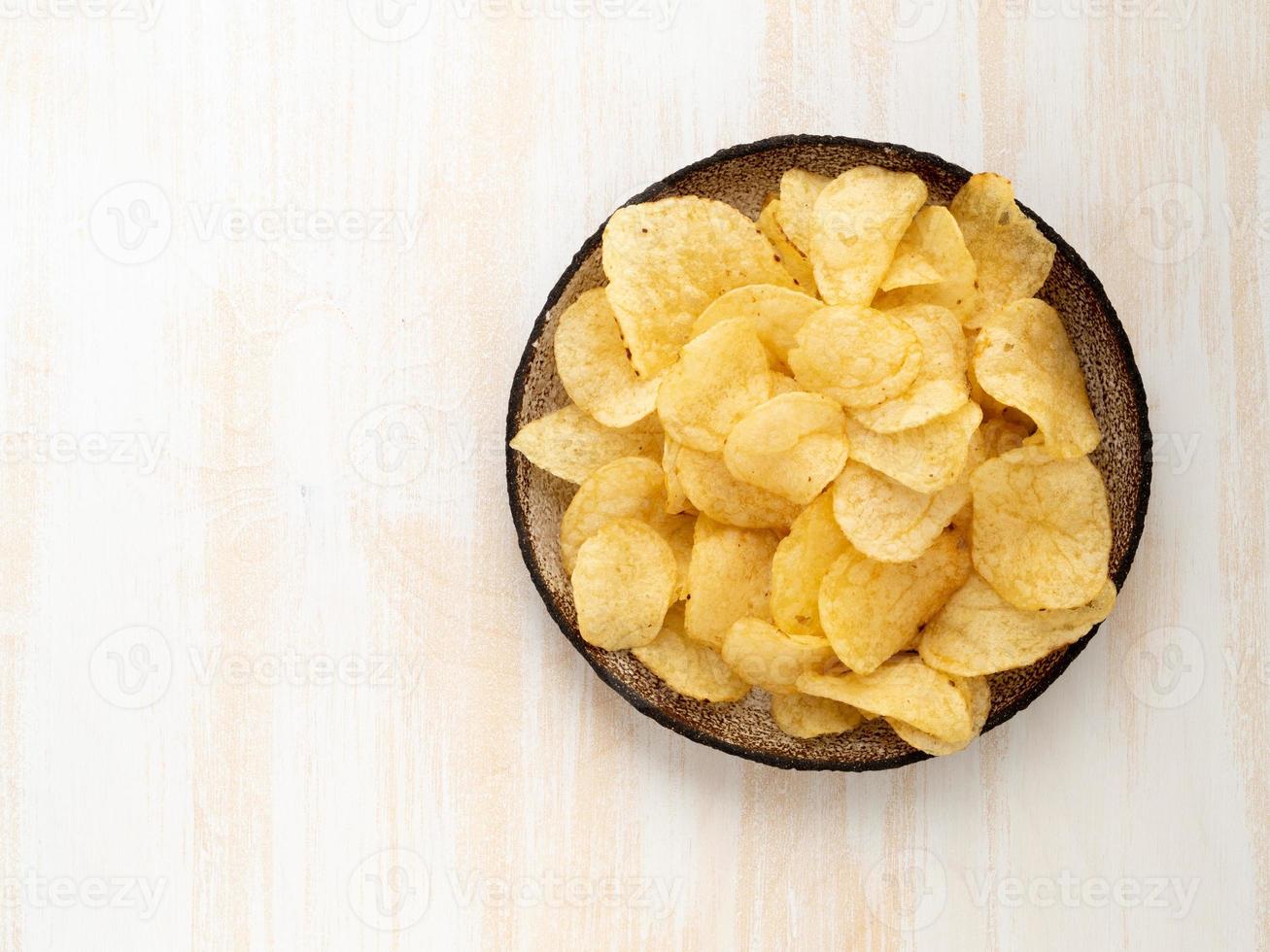 chips amarelos marrons de batata natural em placa de cerâmica marrom sobre fundo branco de madeira foto