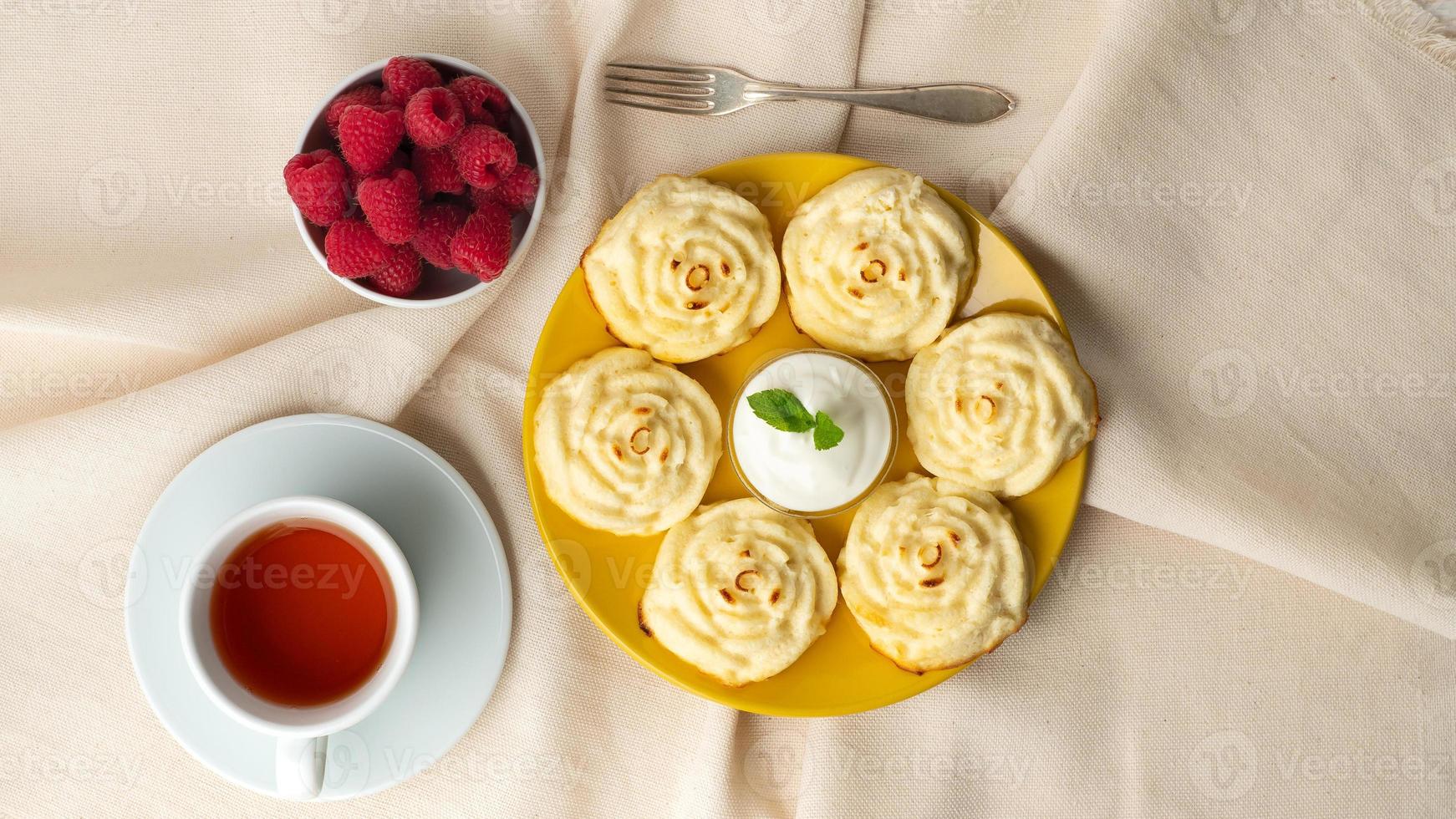 panquecas de queijo diet, forma de rosa, na placa amarela com chá, framboesa em guardanapo de linho têxtil foto