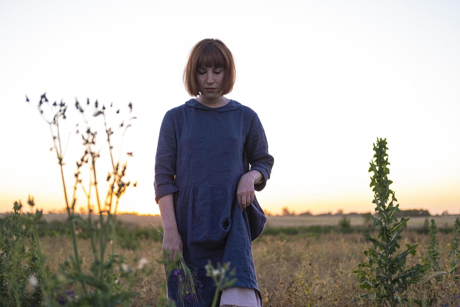 Mulher jovem ruiva com sardas em vestido vintage feito à mão anda em campos com flores foto