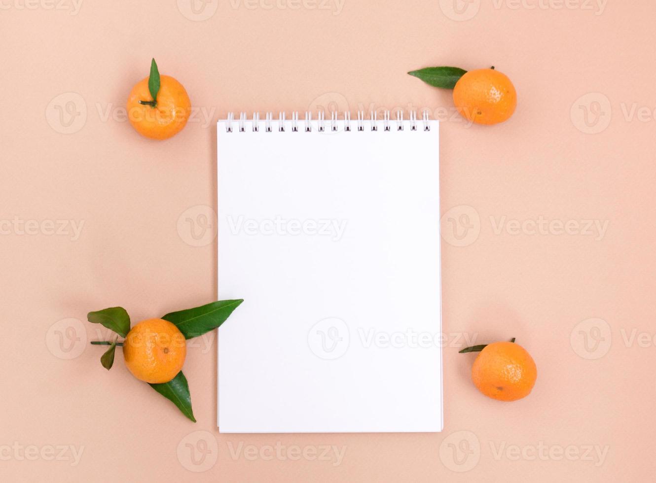 um caderno branco vazio e tangerinas em um fundo de pêssego. modelo com espaço para texto, conceito de planejamento ou maquete. foto