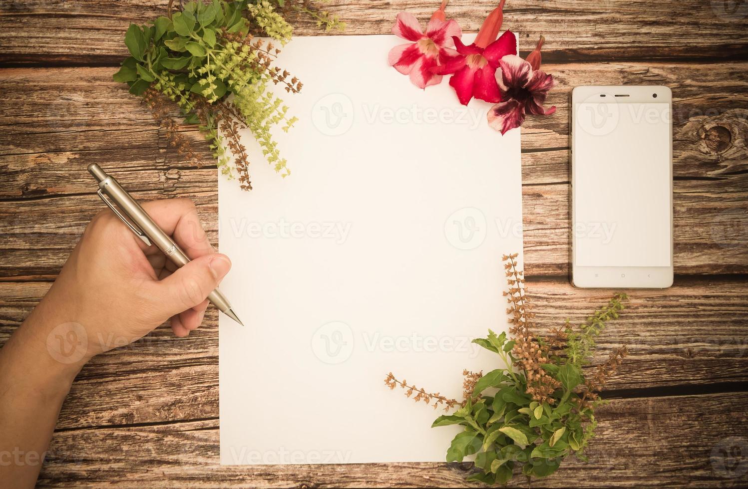 espaço conceitual para texto, que consiste no cabo de uma caneta e escrita móvel em um pedaço de papel em branco, flores de azaléia e manjericão em um fundo de madeira. foto