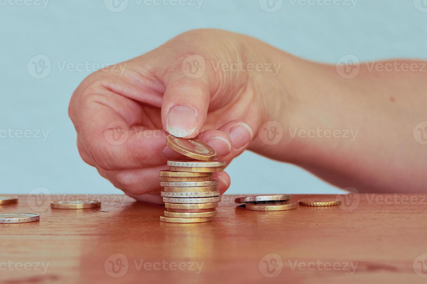 mão de mulher empilha uma e duas moedas de euro em uma torre de moedas foto