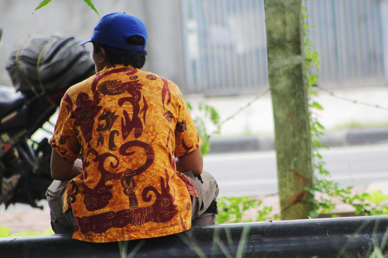 um homem de meia idade está sentado ao lado da rua em jacarta, vestindo roupas de batik indonésio foto