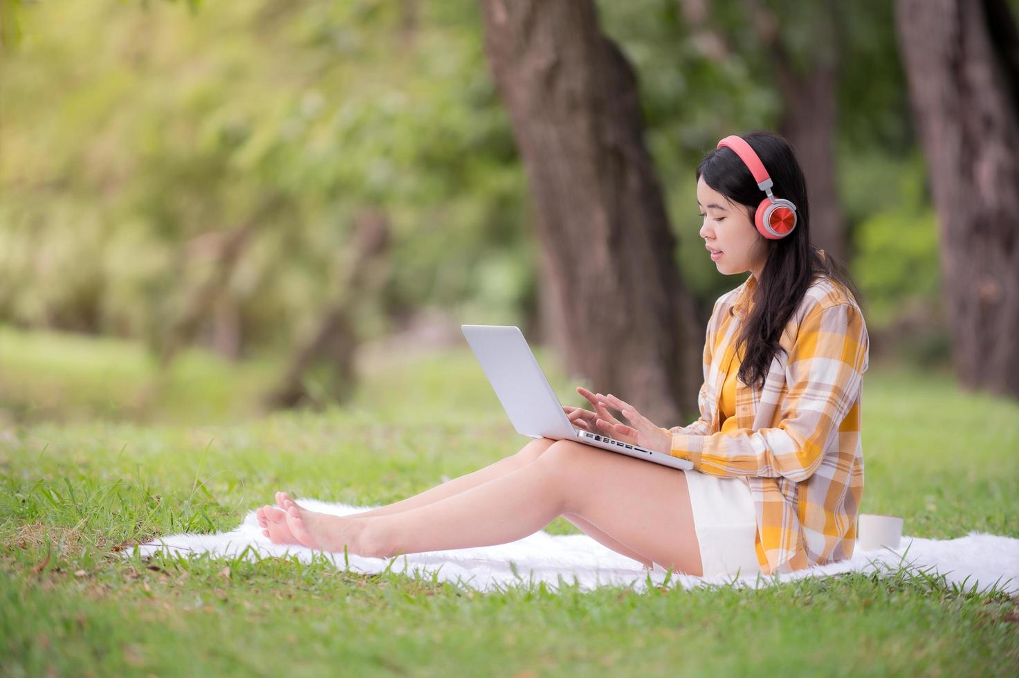 uma linda mulher asiática está relaxando no jardim, lê e procura informações de aprendizado na internet foto