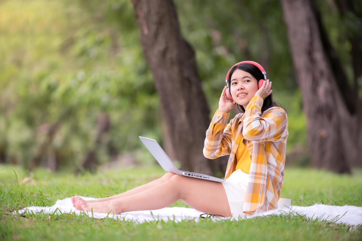 uma linda mulher asiática está relaxando no jardim, lê e procura informações de aprendizado na internet foto