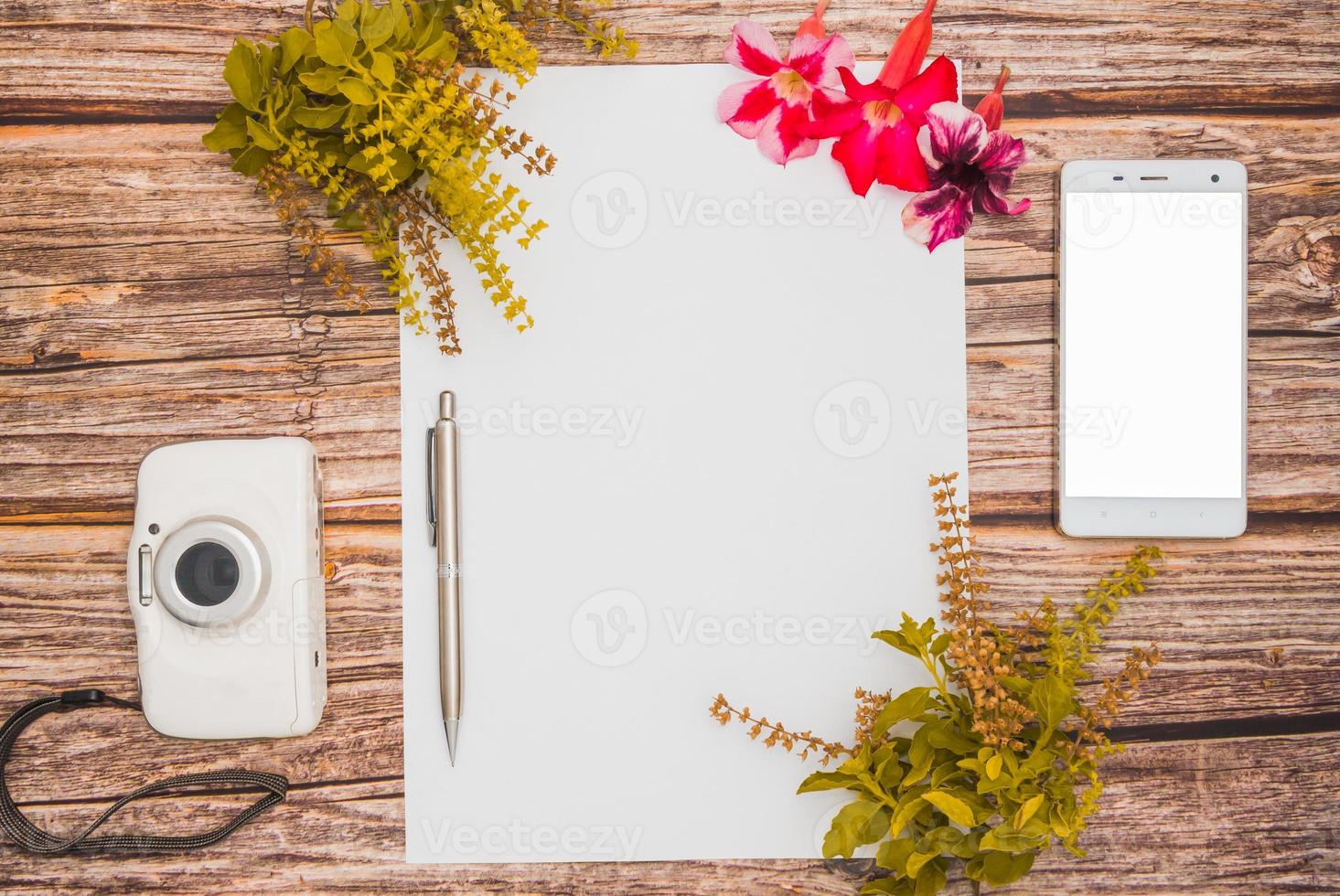 espaço de conceito para texto, que consiste em papel em branco, azaléia, flores de manjericão, telefone celular, caneta e câmera em um fundo de madeira. modelo em branco para seu text.top view.flat lay foto