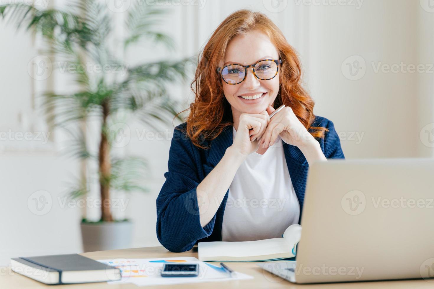 satisfeito alegre economista ruiva desenvolve projeto de inicialização financeira, posa no interior do escritório, trabalha na esfera de negócios, vestido com roupas formais, tem expressão feliz, possui empresa foto