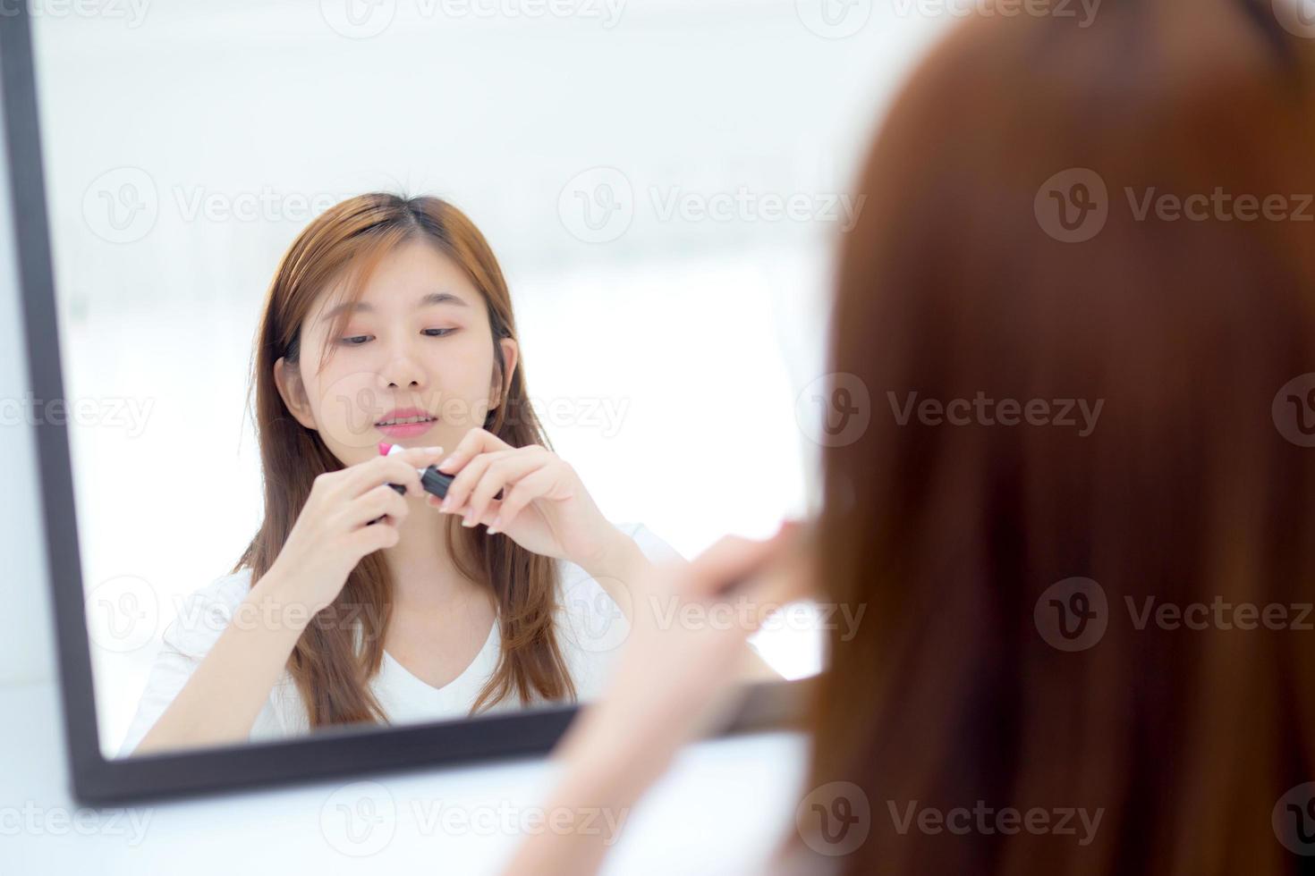 beleza do retrato de uma jovem mulher asiática no espelho segurando e olhando um batom de maquiagem, moda de beleza linda garota na sala, conceito de estilo de vida. foto