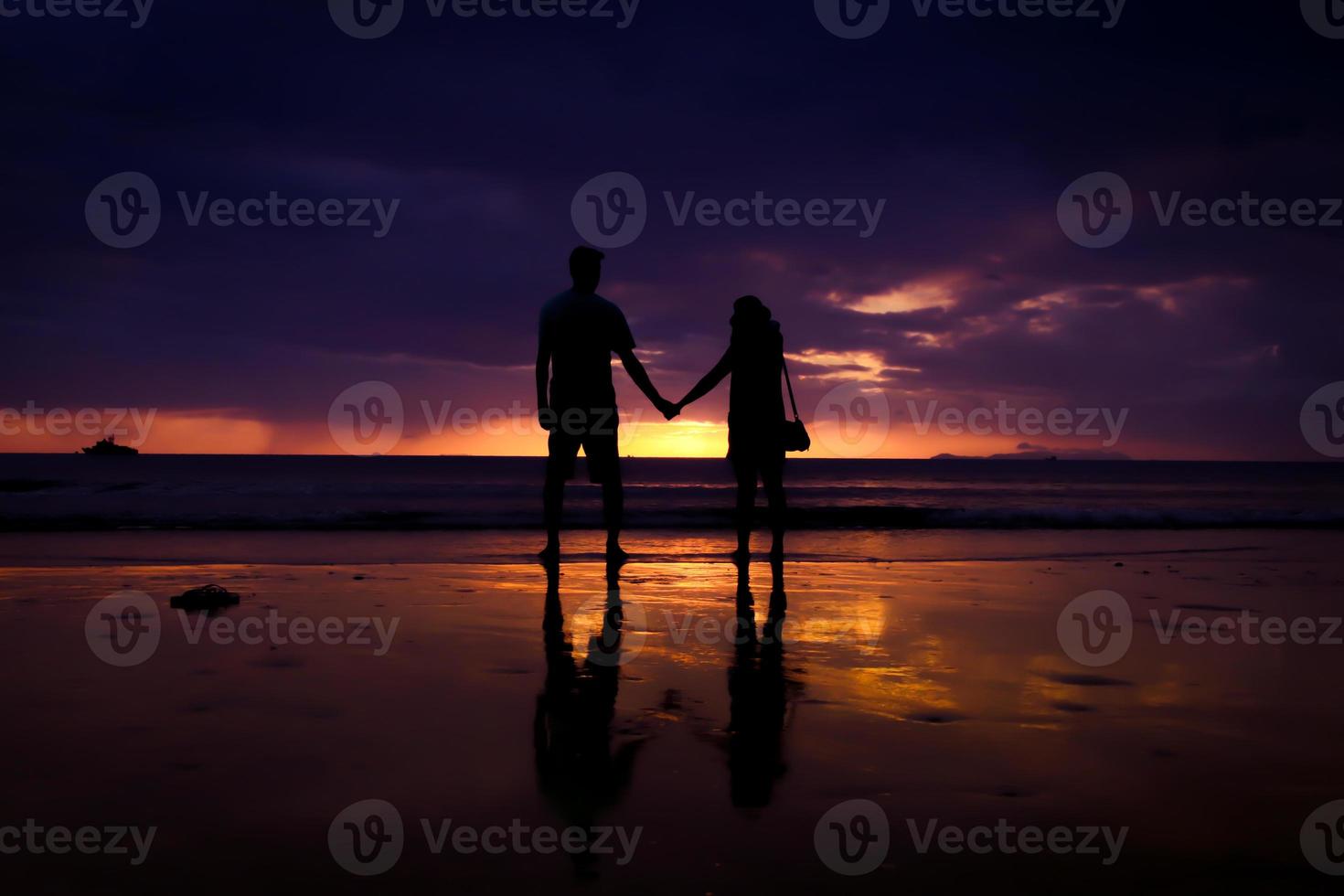 silhueta de casal se abraçam e feliz casal jovem ama na praia na hora do pôr do sol foto