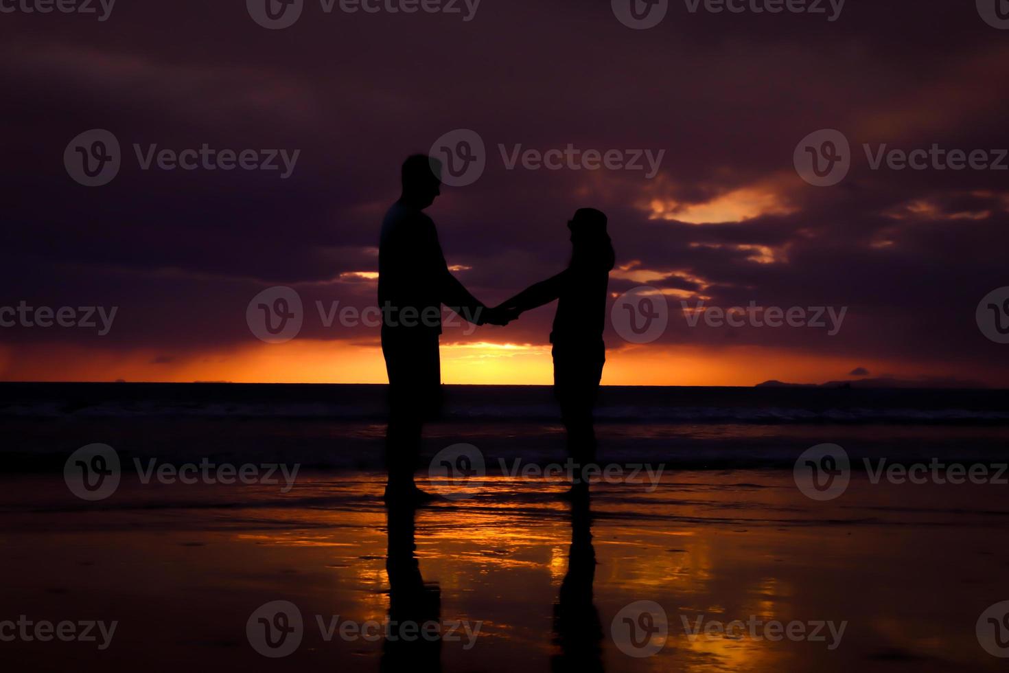 silhueta de casal se abraçam e feliz casal jovem ama na praia na hora do pôr do sol foto