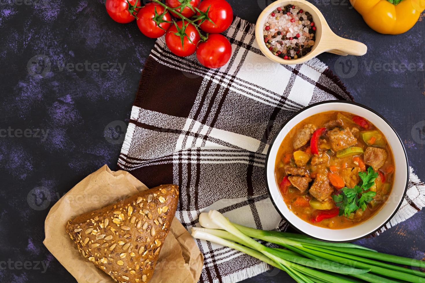 ensopado com carne e legumes em molho de tomate em fundo escuro foto