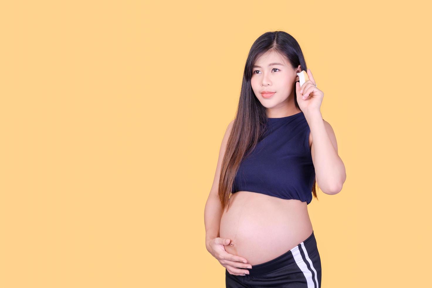 uma linda mulher asiática grávida toca sua barriga e usa um termômetro de ouvido para medir a febre foto