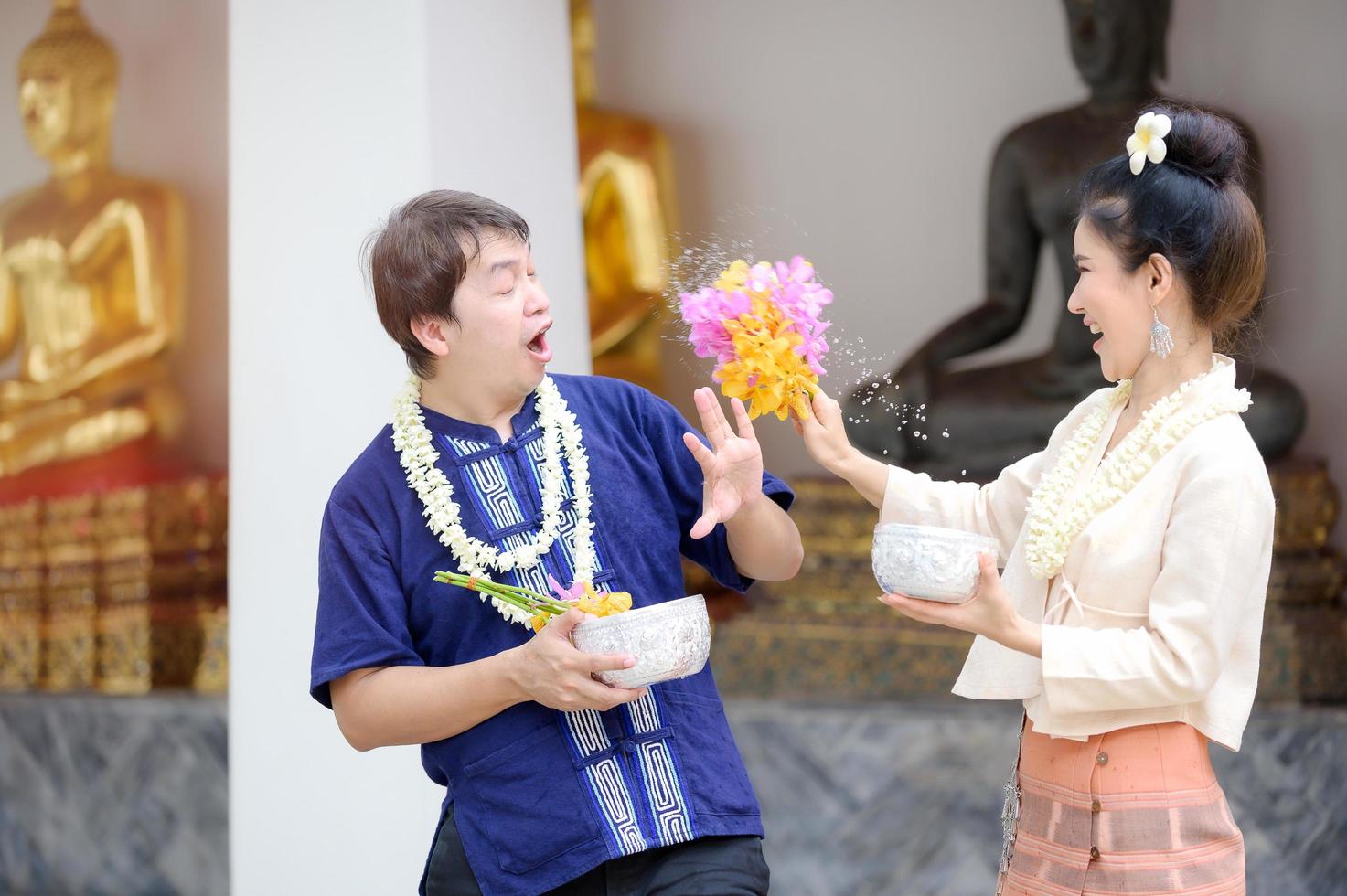 homens e mulheres tailandeses jovens em vestido tailandês tradicional seguram flores espirrando água para se divertir no festival de água songkran foto