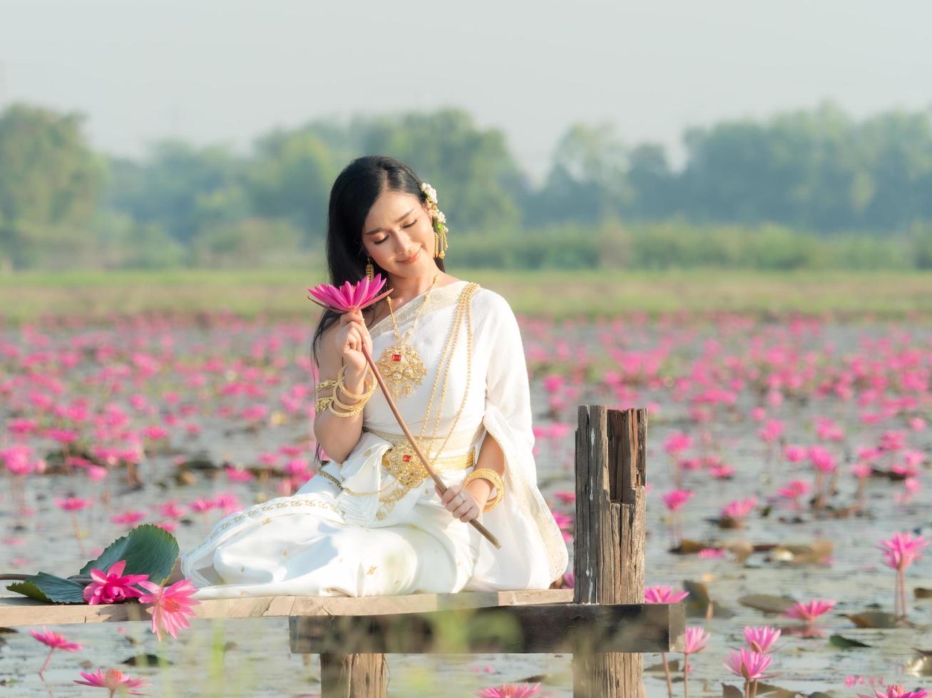 uma elegante mulher tailandesa vestindo roupas tradicionais tailandesas carregando folhas de flores de lótus coletadas de um campo de lótus foto