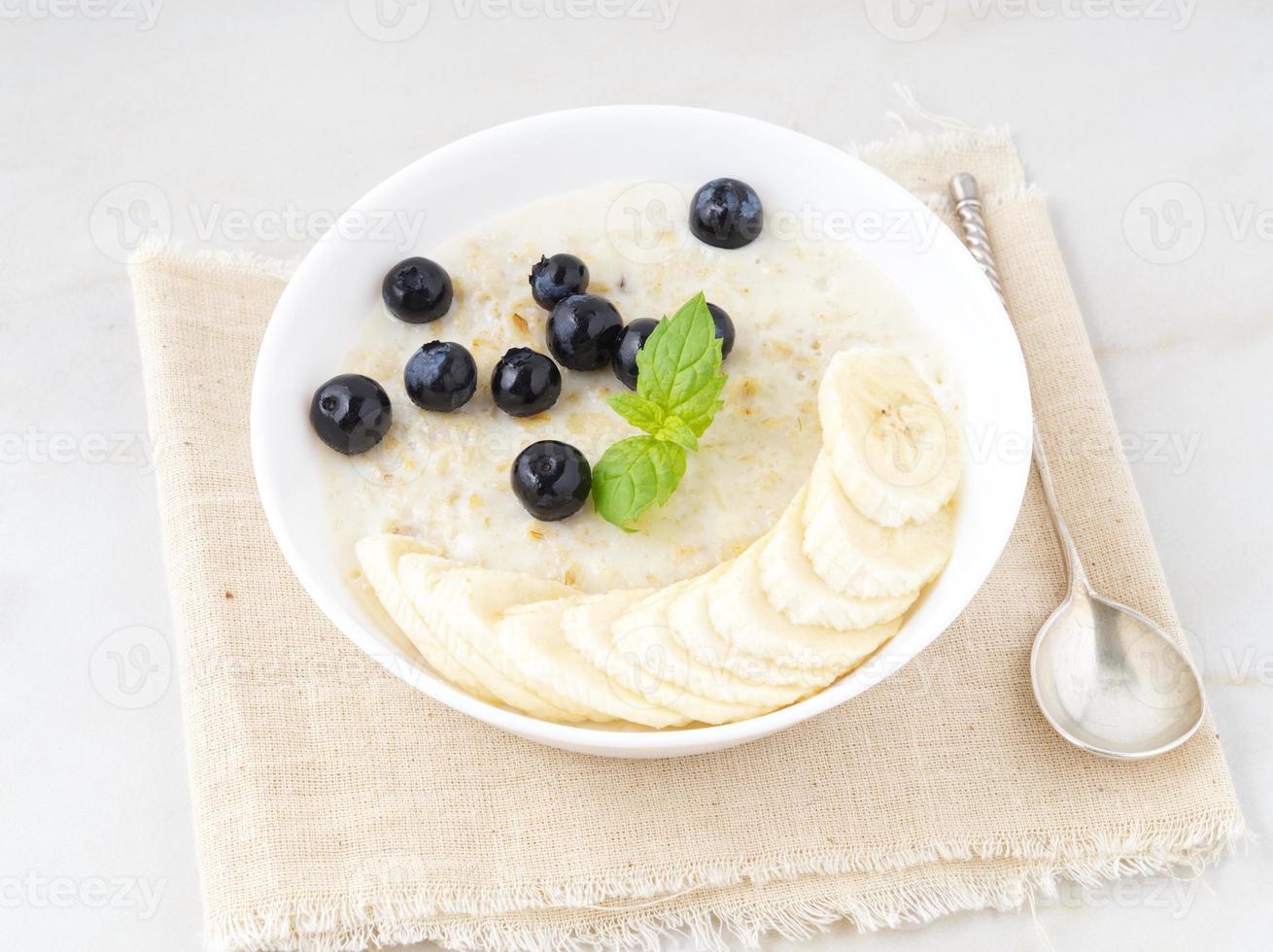 tigela grande de aveia saborosa e saudável com frutas e bagas no café da manhã, refeição matinal. vista lateral, mesa de mármore branco foto