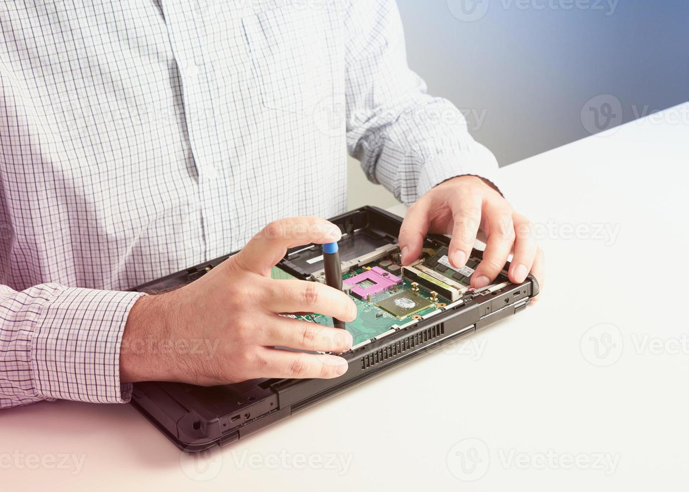 homem repara computador. um engenheiro de serviço em laptop de reparos de camisa, na mesa branca contra a parede branca. foto