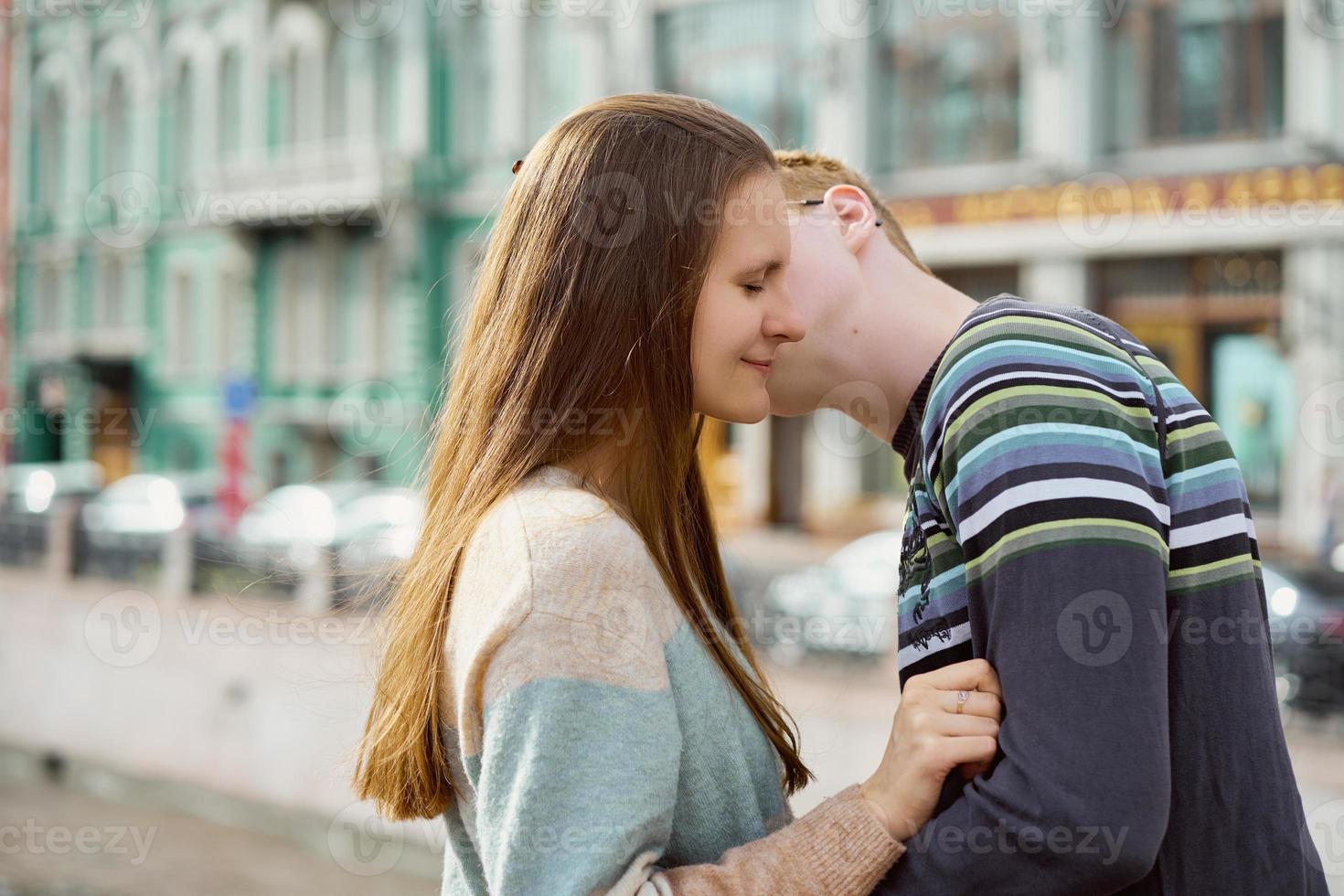 retrato de casal feliz abraçando no centro da cidade, homem ruivo com óculos beija ou sussurra mulher com cabelo comprido foto