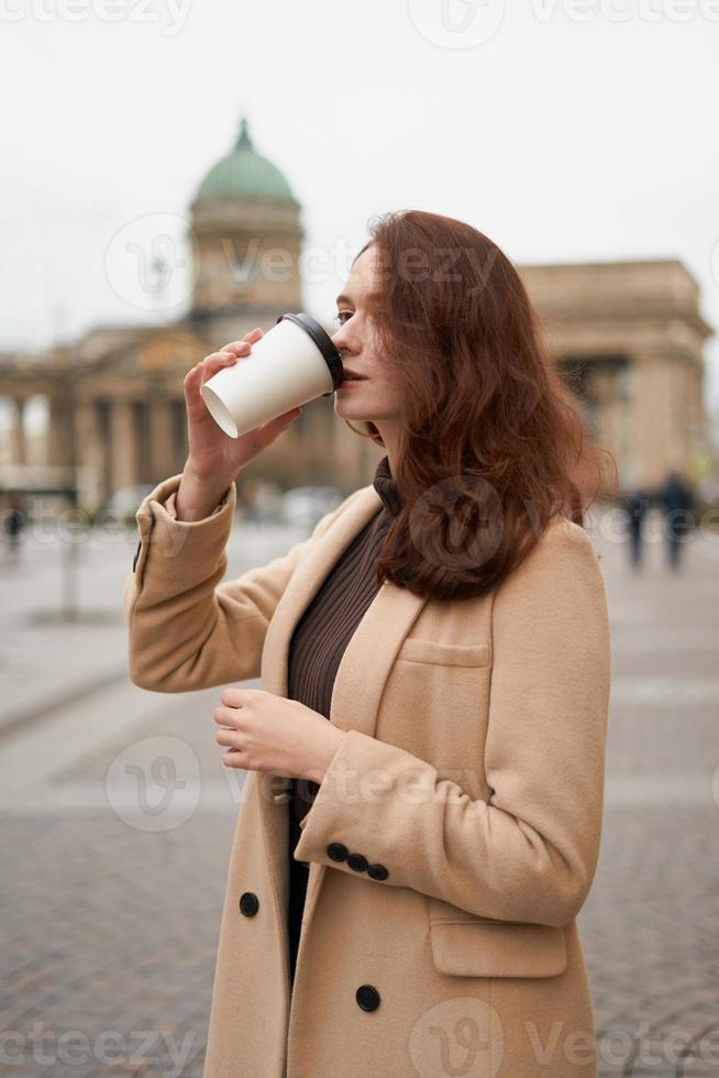 linda elegante elegante elegante garota bebe café, vai andando pela rua de st. petersburgo no centro da cidade. encantadora mulher pensativa com longos cabelos escuros foto