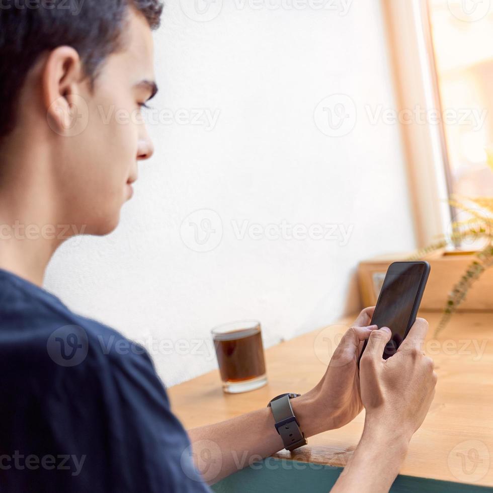 jovem adulto olhando para o celular, sentado no café. idade digital. as pessoas se comunicam no chat. foto