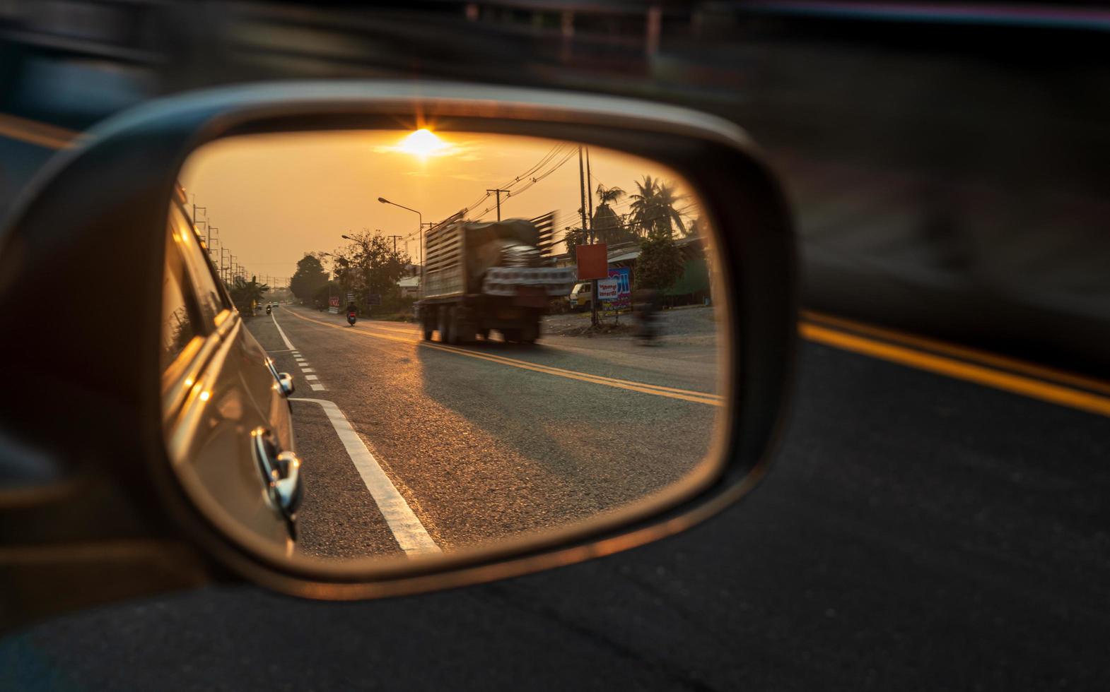 um close-up, o reflexo dos espelhos laterais do carro com o sol alaranjado da manhã nascendo. foto