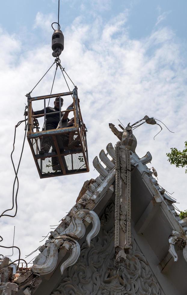 vista baixa, trabalhadores em cestas de aço acima de telhados tailandeses padronizados. foto