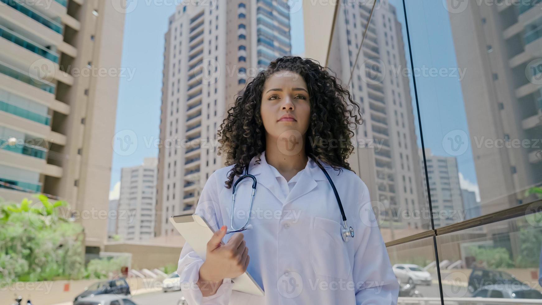 jovem médica latina usa uniforme branco, usando tablet digital no hospital foto