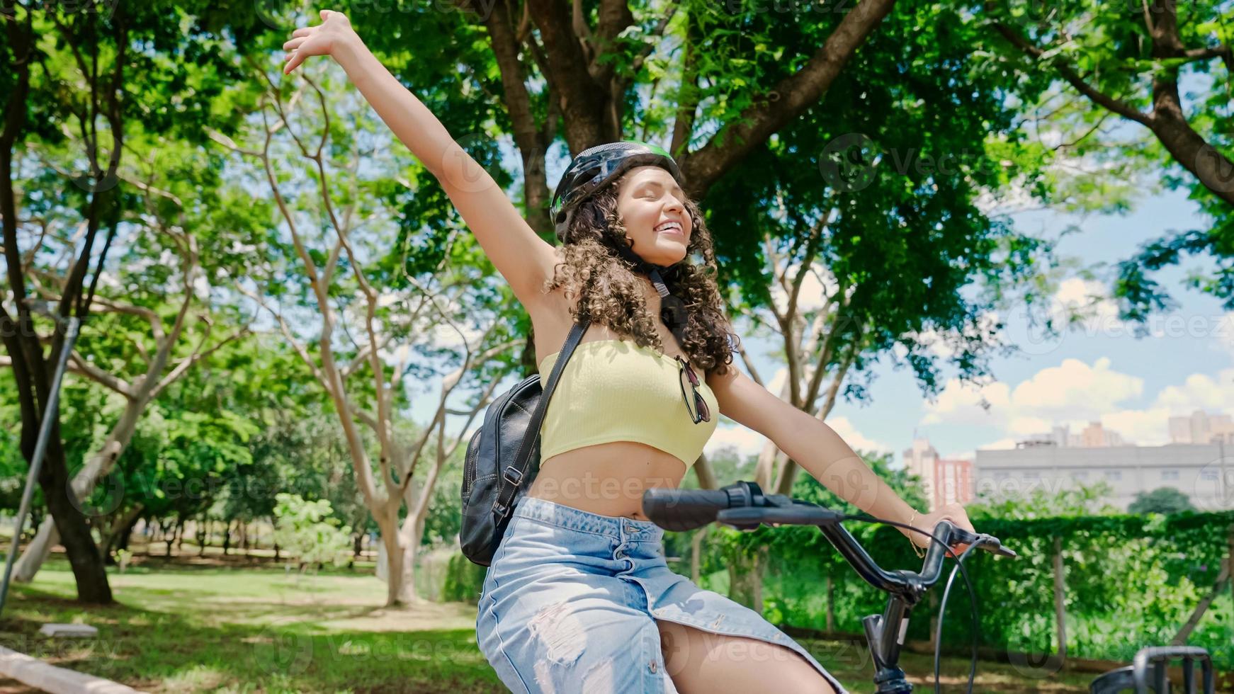 jovem latina no capacete protetor está andando de bicicleta ao longo da ciclovia em um parque da cidade foto