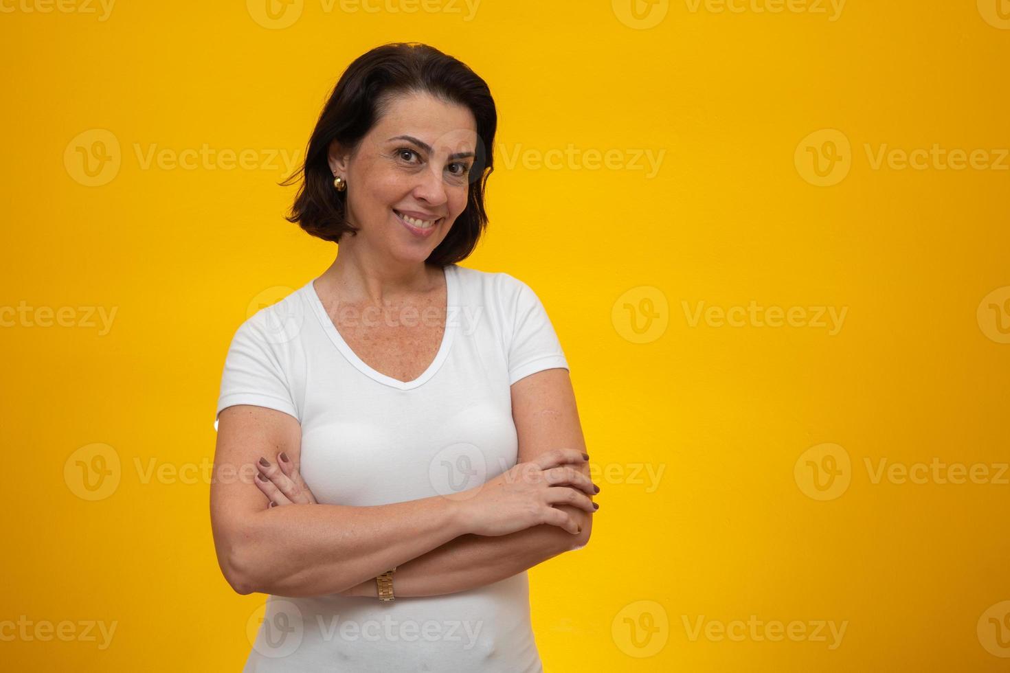 mulher de meia idade atraente com braços cruzados em fundo amarelo foto