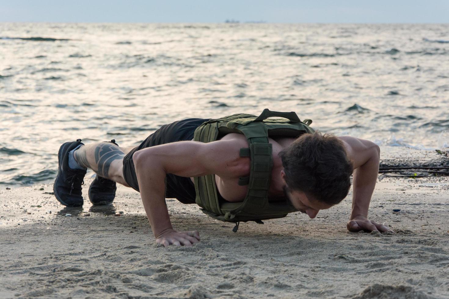 jovem atleta barbudo treinando ao ar livre com colete ponderado, exercício com portador de placa militar foto