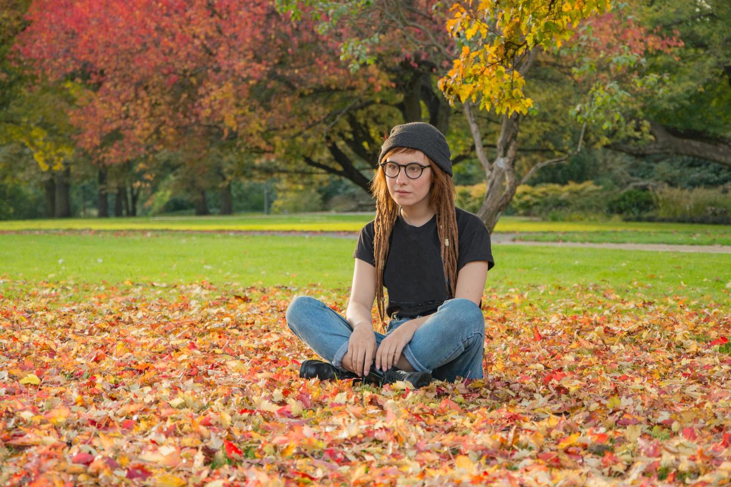 jovem mulher com dreadlocks vermelhos e óculos relaxantes no parque outono foto