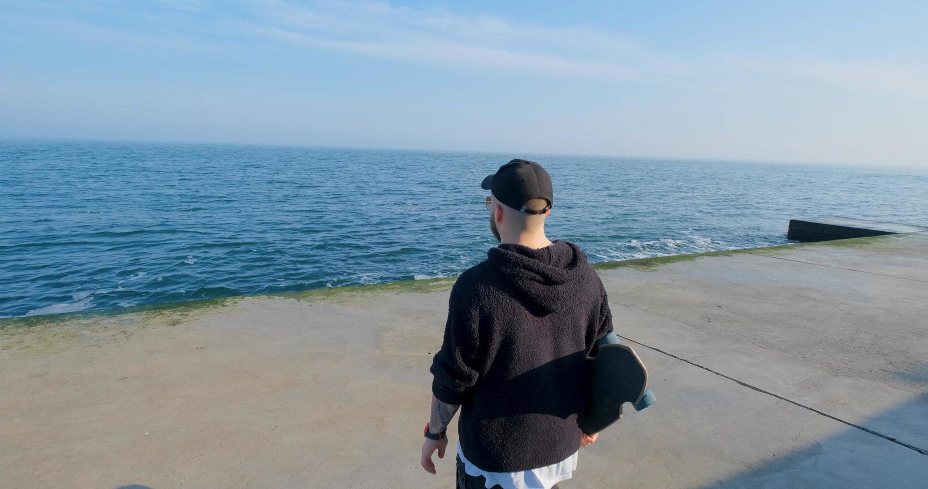 jovem macho com skate relaxante perto do mar foto