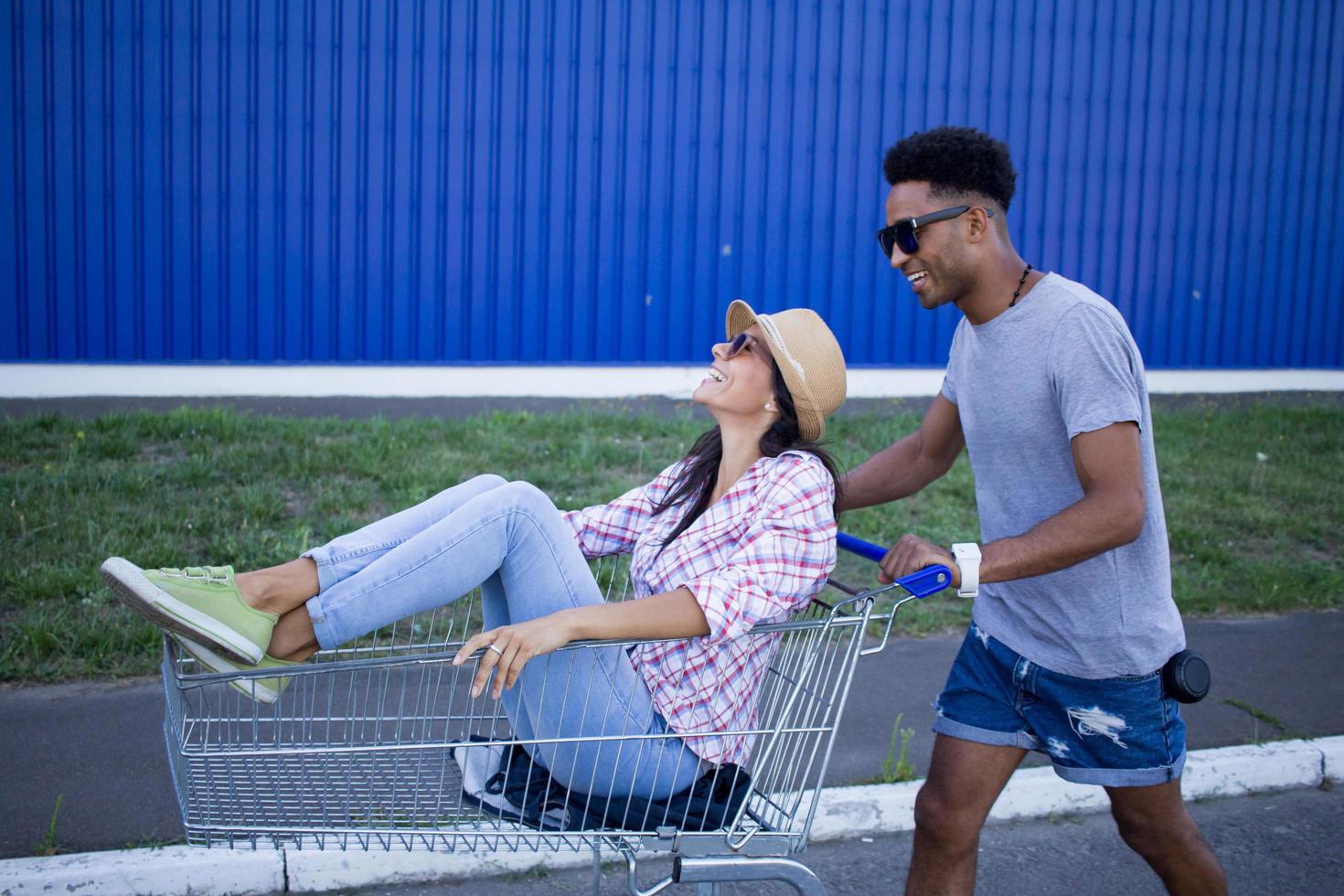 casal jovem feliz andando de carrinho no estacionamento vazio do shopping, amigo hipster se divertindo durante as compras, casal apaixonado andando no carrinho de compras foto