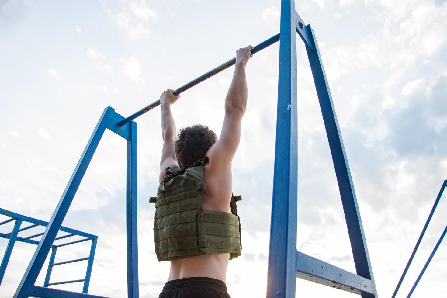 jovem atleta barbudo treinando ao ar livre com colete ponderado, exercício com portador de placa militar foto