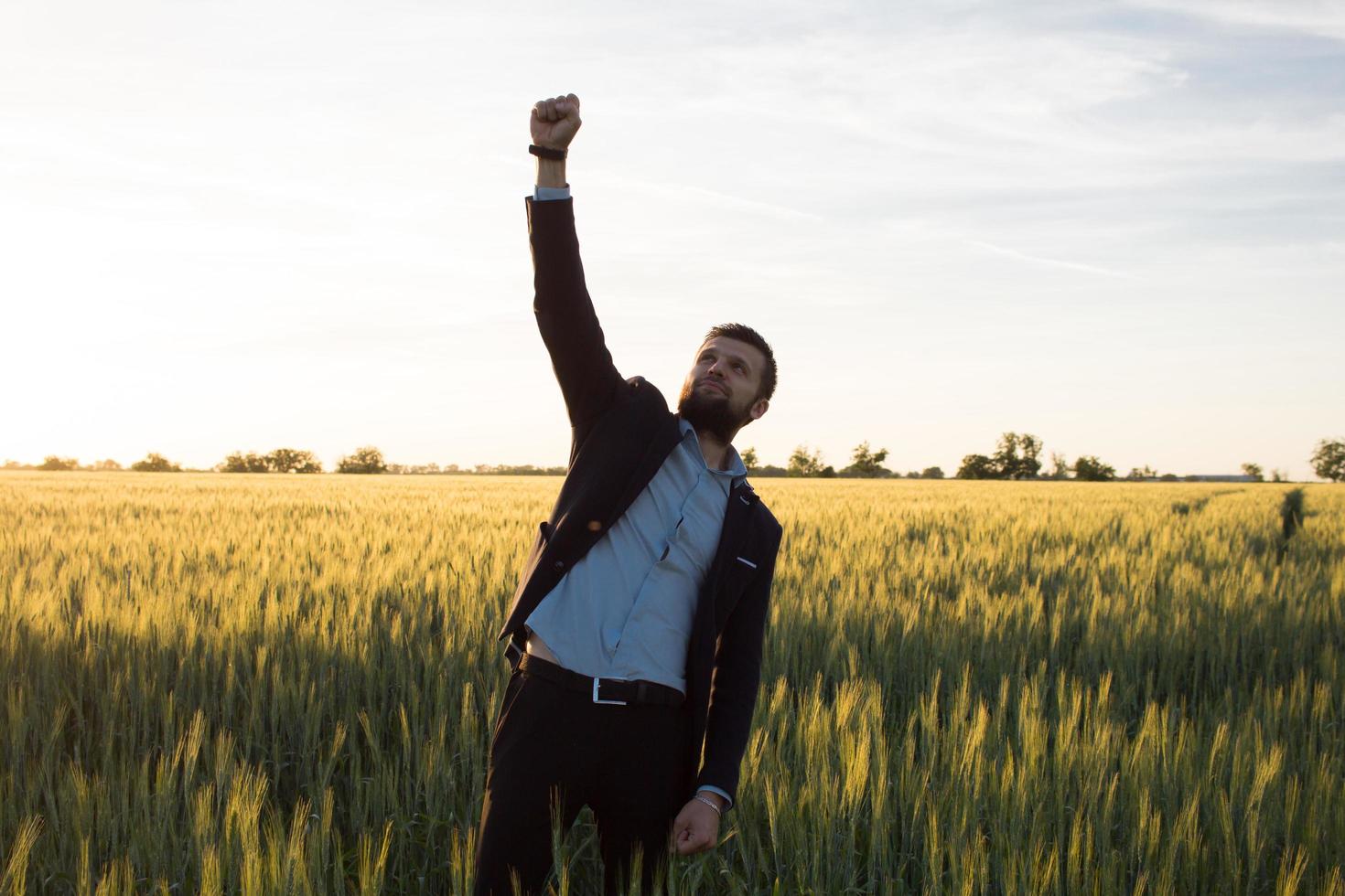 conceito de vencedor, feliz jovem empresário saltar com as mãos levantadas nos campos, plantas de trigo de verão foto