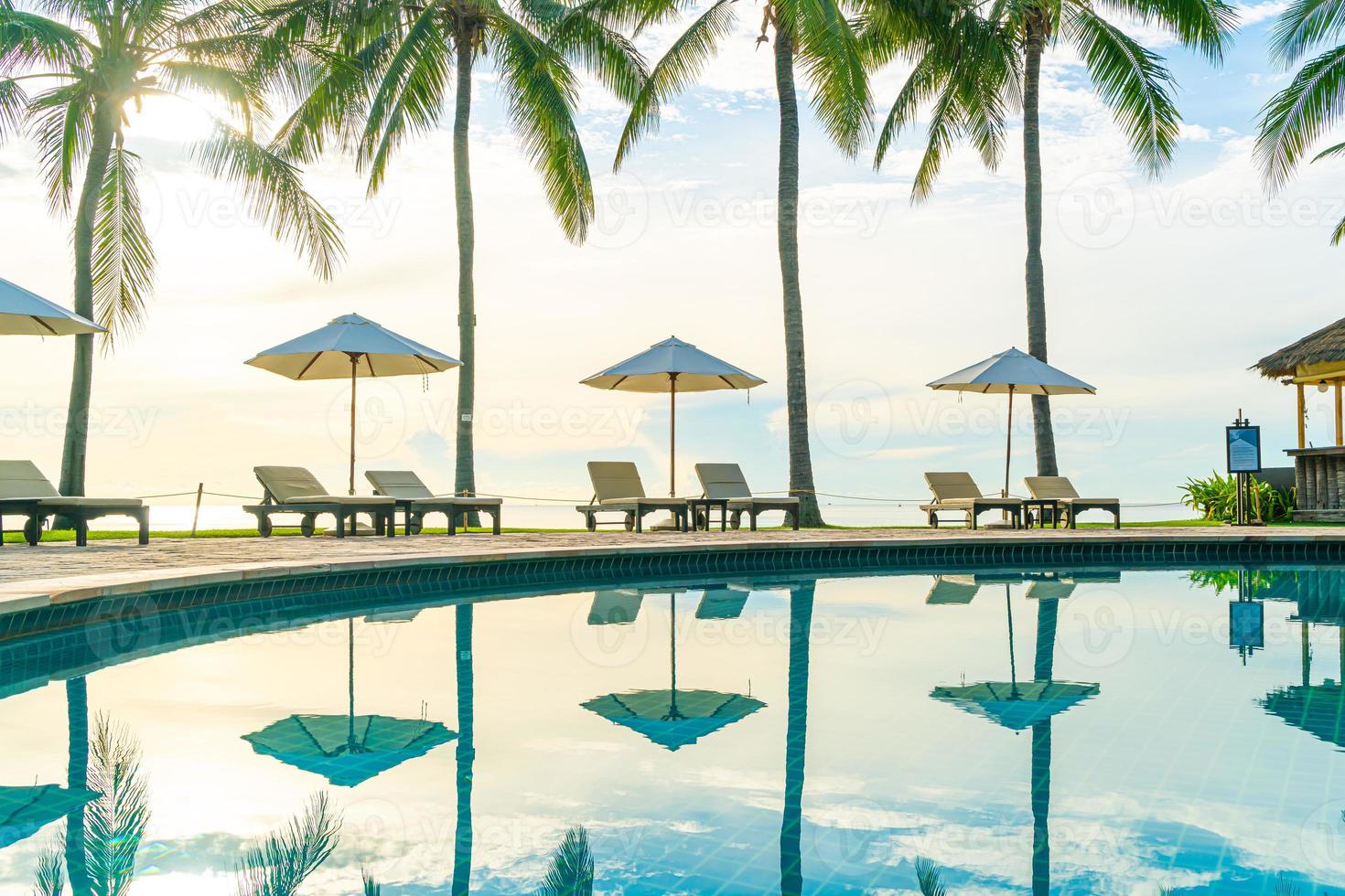 belo guarda-sol de luxo e cadeira ao redor da piscina ao ar livre em hotel e resort com coqueiro no céu do pôr do sol foto