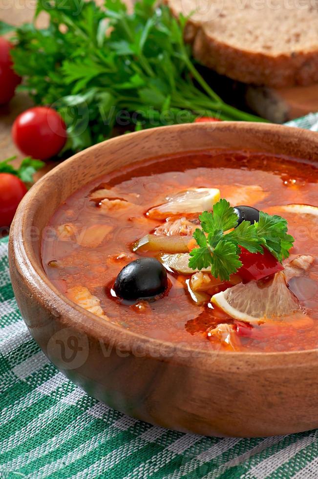 sopa solyanka russo com carne, azeitonas e pepinos em tigela de madeira foto