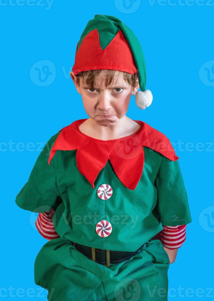 menino carrancudo vestido como elfo de natal em fundo de tela azul foto