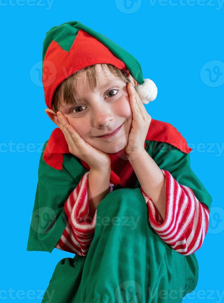 menino feliz sorridente vestido como elfo de natal em fundo de tela azul foto