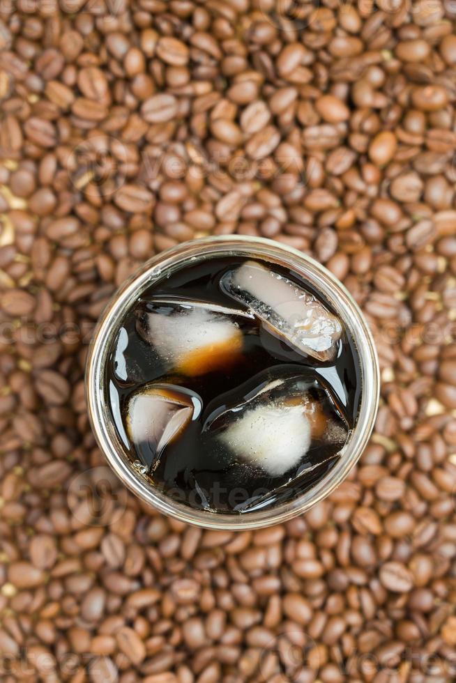 xícara de café de americano gelado na mesa em fundo texturizado de grãos de café torrados. vista superior café preto com espaço para texto foto