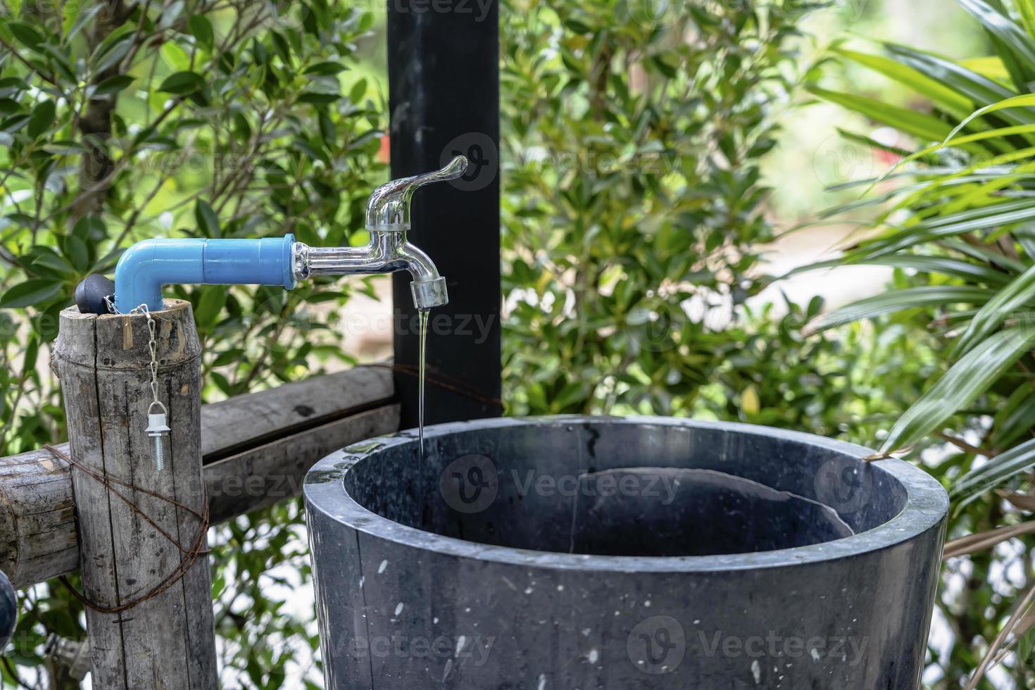 close-up de uma torneira de água ou torneira vazando gota de água com lavatório de fundo verde no banheiro ou parque. conservação de água ou conceito de economia foto