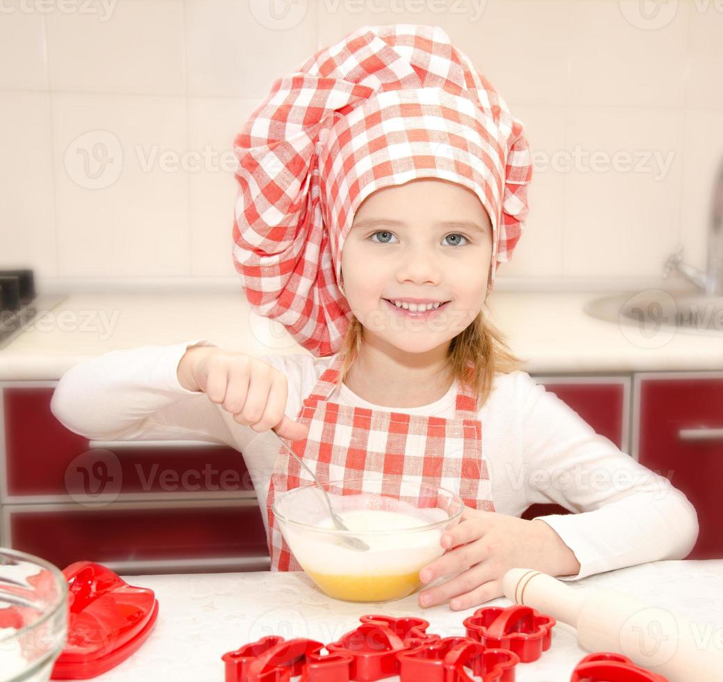 menina sorridente com chapéu de chef mexendo a massa de biscoitos foto