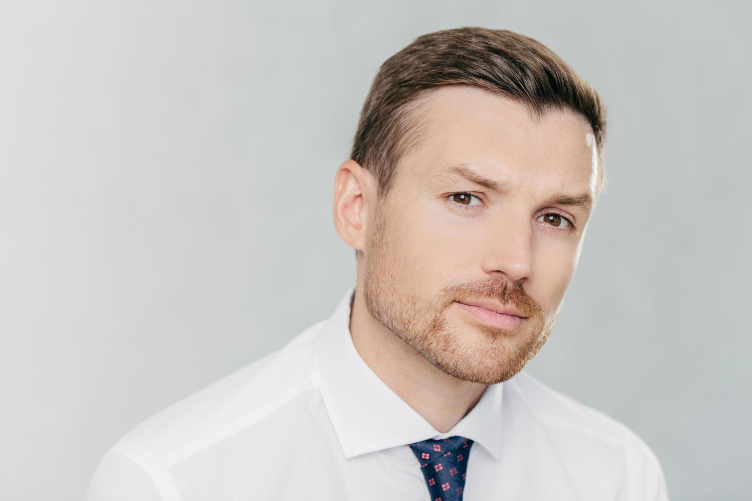 close-up retrato de homem bonito com barba olha seriamente para a câmera, tem um olhar atraente, pensa em negócios, vestido com roupas formais, isolado sobre fundo branco. CEO interno foto