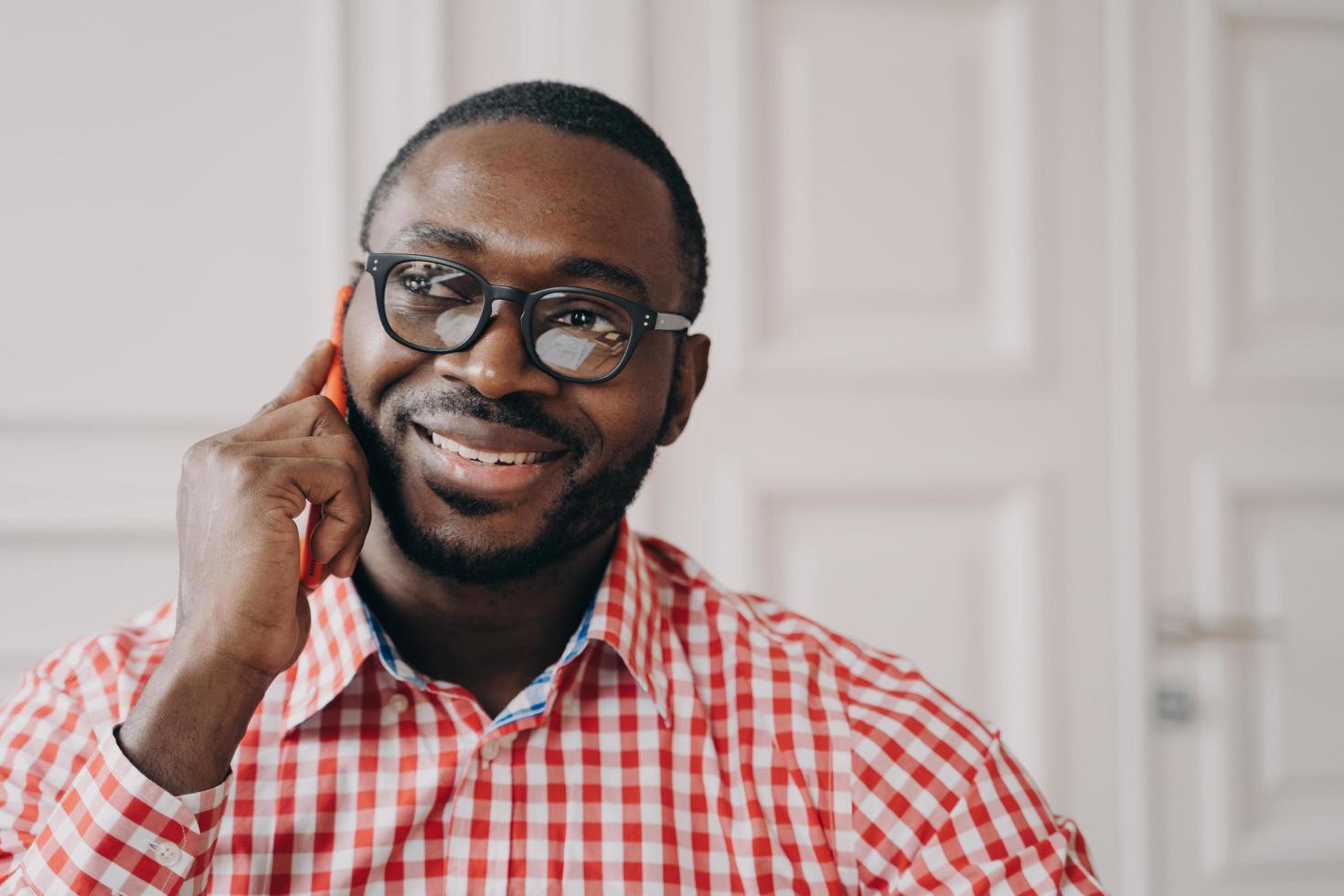 sorridente homem africano alegre freelancer falando no celular enquanto trabalhava remotamente foto