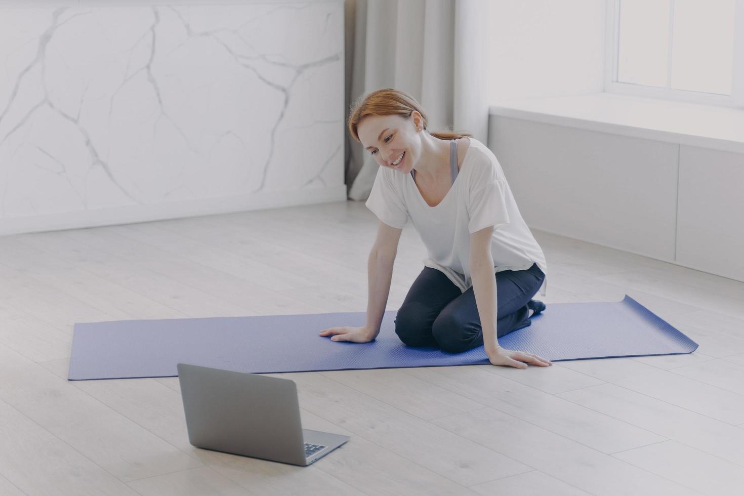 mulher caucasiana feliz tem treinamento pessoal à distância na frente da câmera no tapete de ioga no chão. foto
